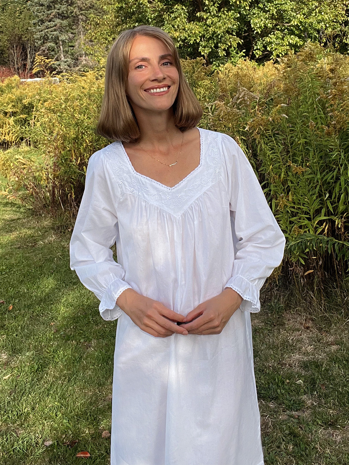 Woman in a white dress standing outdoors with greenery in the background