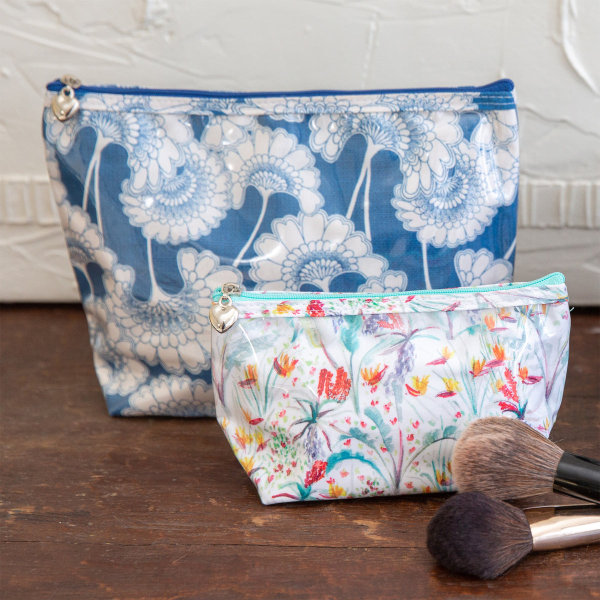 Two floral-patterned makeup bags on a wooden surface with brushes.
