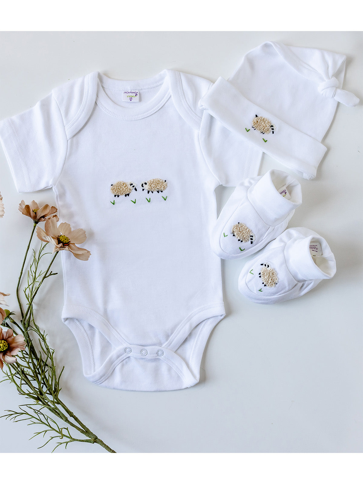 Baby clothing set with onesie, hat, and booties on a light background with flowers.