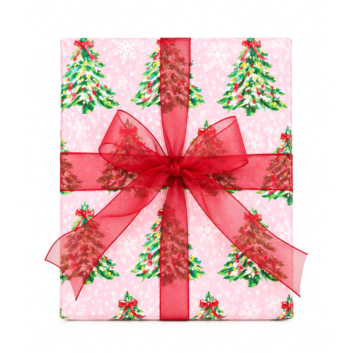 A square gift box wrapped in pink holiday paper with a repeating pattern of green Christmas trees and white snowflakes, tied with a large sheer red ribbon and bow in the center, on a plain white background.