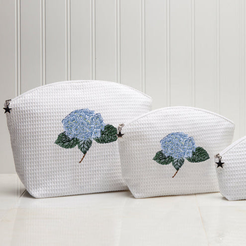 Three white textured pouches with floral designs on a light wooden background