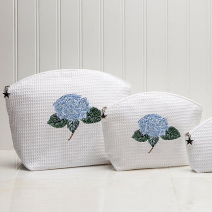 Three white textured pouches with floral designs on a light wooden background