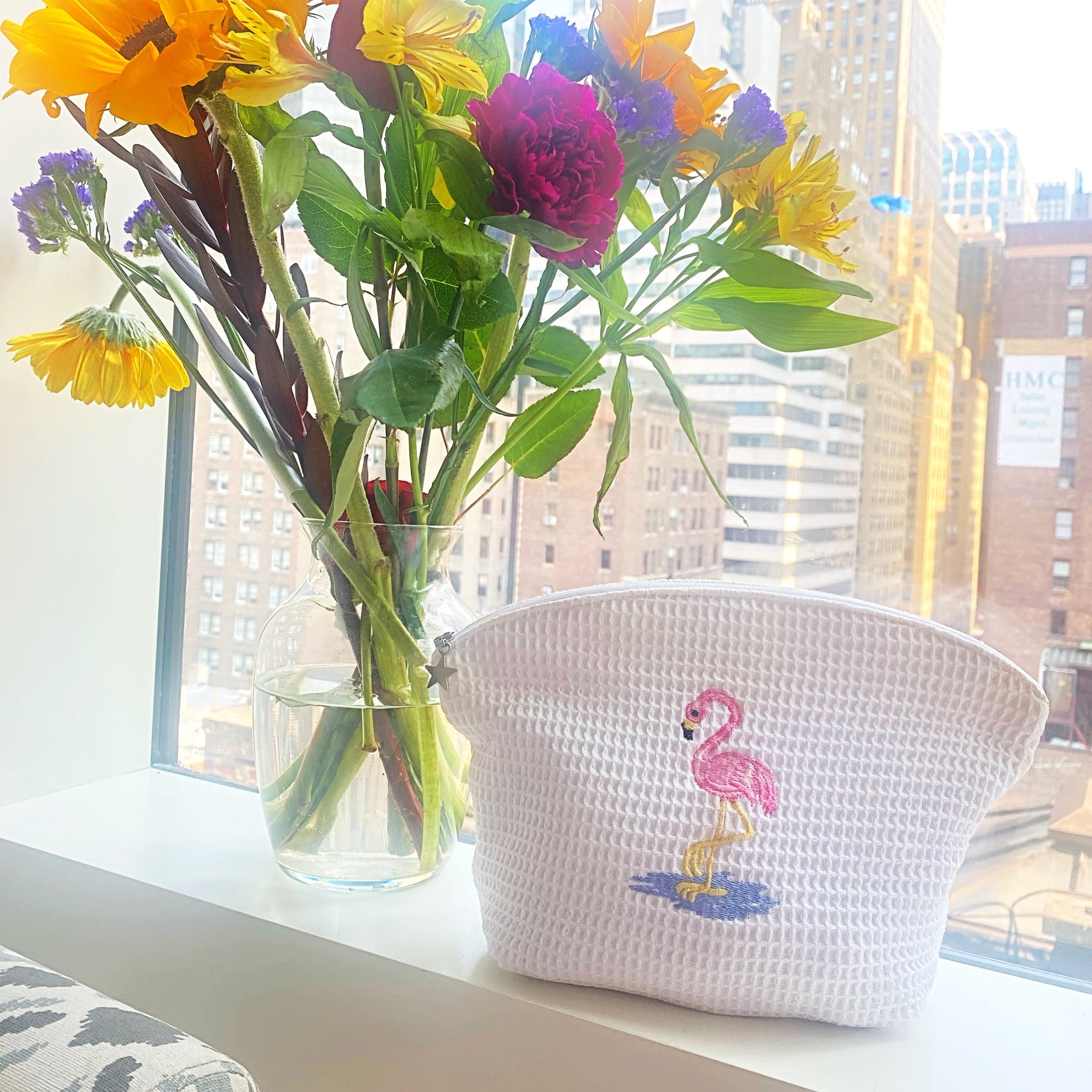 Colorful flowers in a vase on a windowsill with a flamingo-themed pouch.