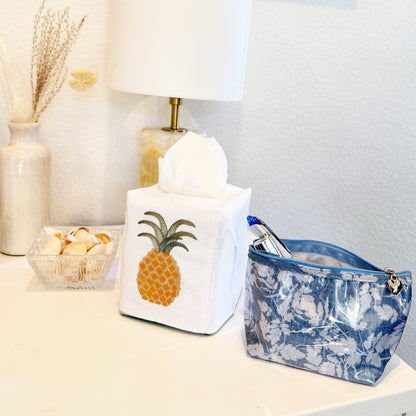 Tissue box with pineapple design on a nightstand next to a lamp and decorative items.
