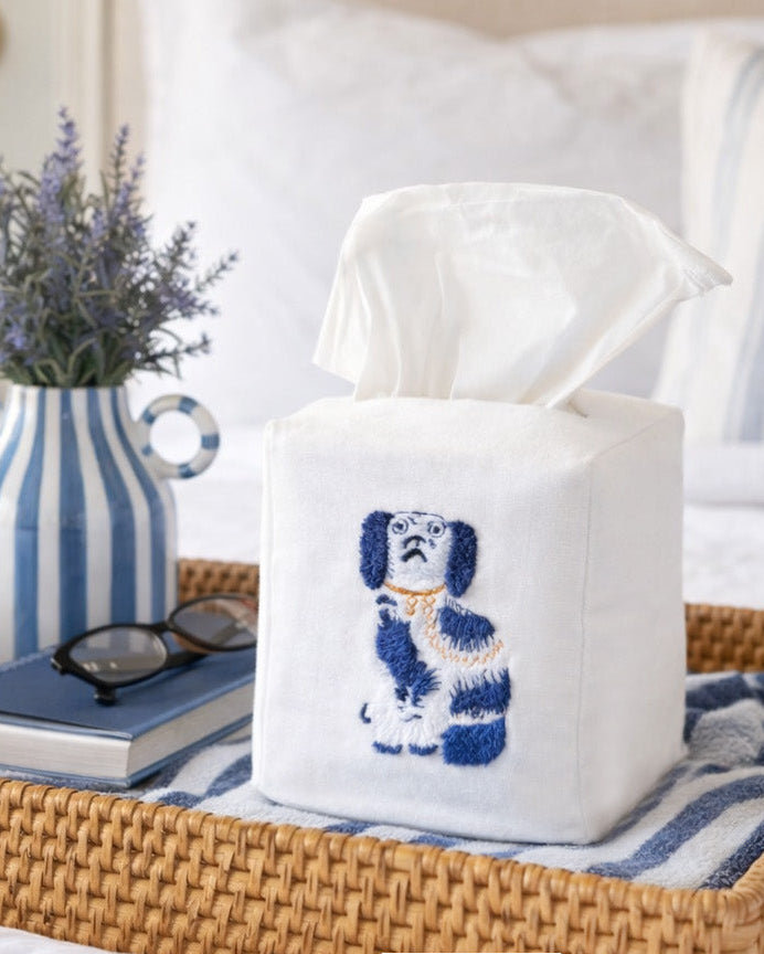 Tissue box cover with embroidered dog design on a table with books and a vase.