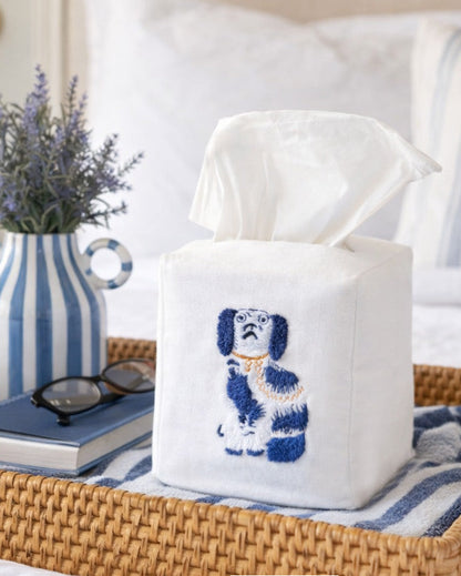 Tissue box cover with embroidered dog design on a table with books and a vase.