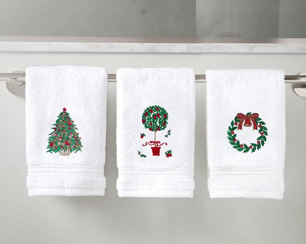 Three white towels with embroidered Christmas designs on a towel rack.