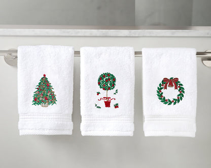 Three white towels with embroidered Christmas designs on a towel rack.