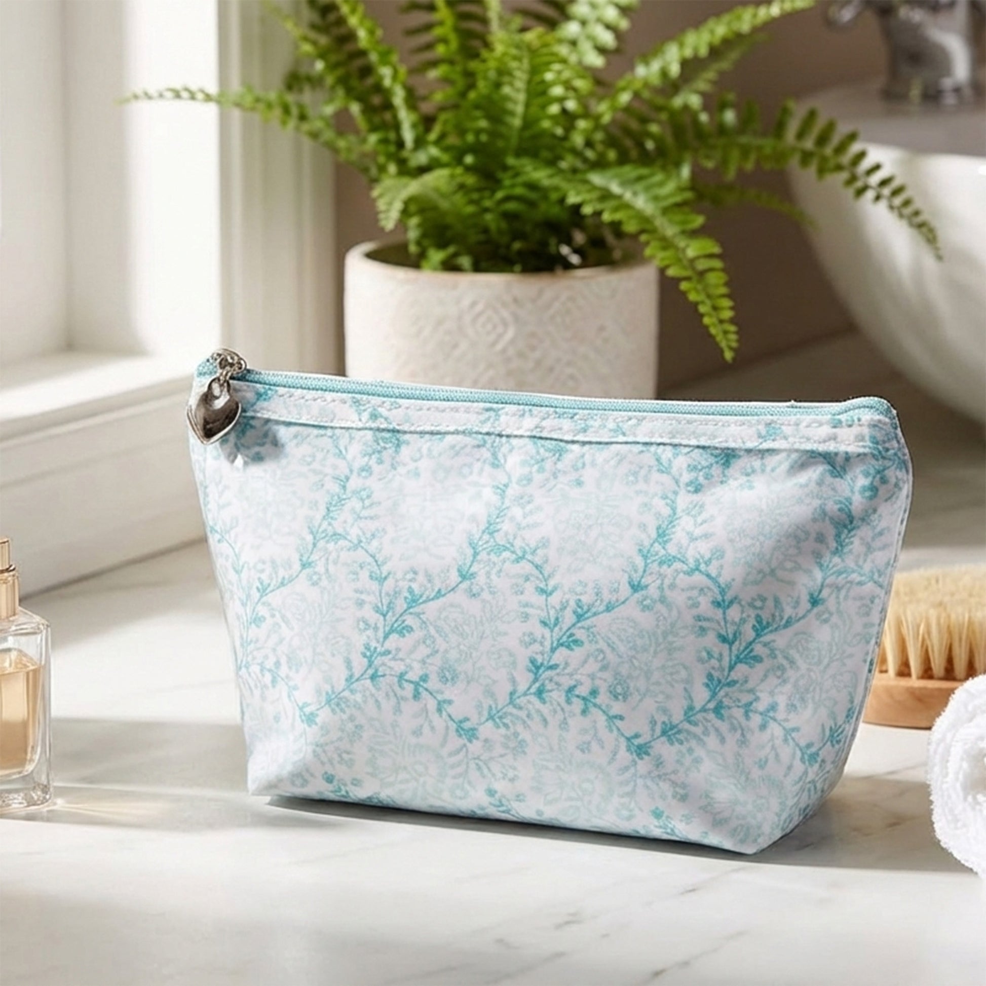 Cosmetic bag with floral pattern on a bathroom counter with a plant and toiletries in the background.