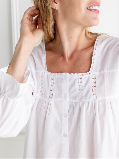 Woman wearing a white blouse with lace details against a light background
