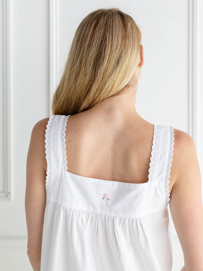 Woman wearing a white sleeveless top with a small pink detail, standing against a white wall.