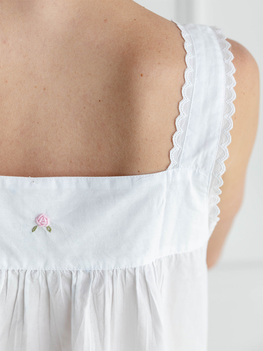 White sleeveless top with scalloped edge and embroidered rose detail on a plain background