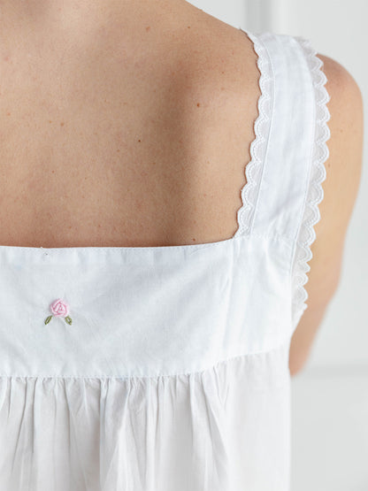 White sleeveless top with scalloped edge and embroidered rose detail on a plain background