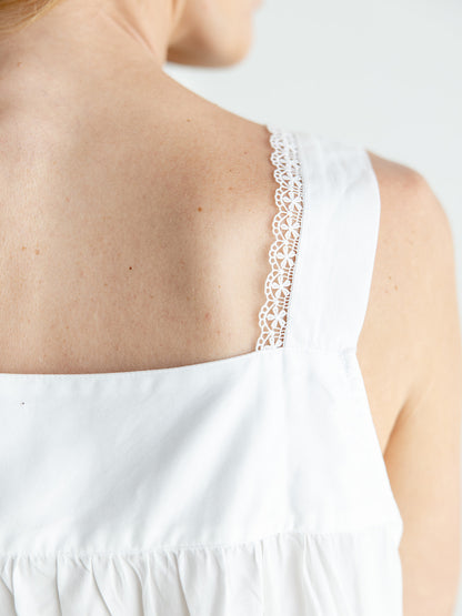Close-up of a person's upper back wearing a white sleeveless cotton nightgown with a decorative white lace trim along the shoulder strap.