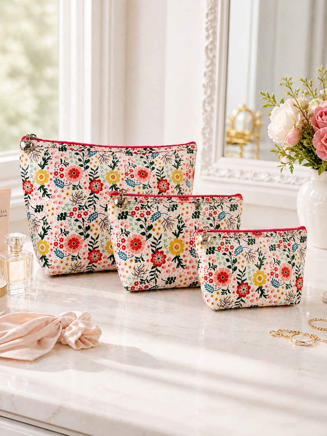 Set of floral-patterned makeup bags on a vanity table with a mirror and flowers in the background.
