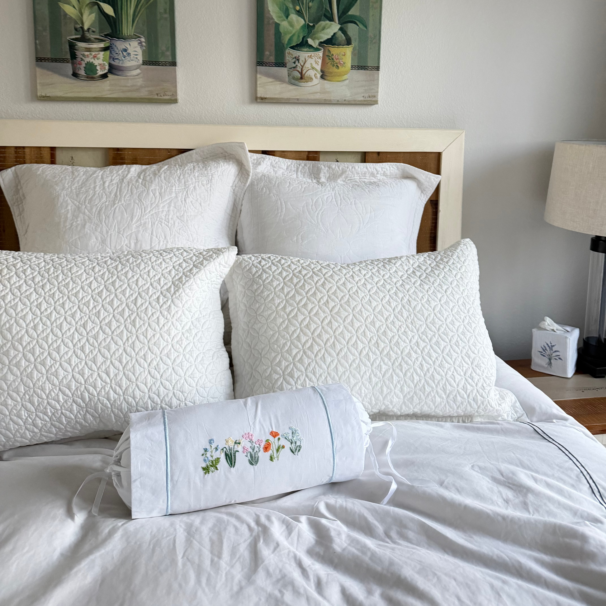 Bedroom with white bedding, floral pillow, and decorative wall art.