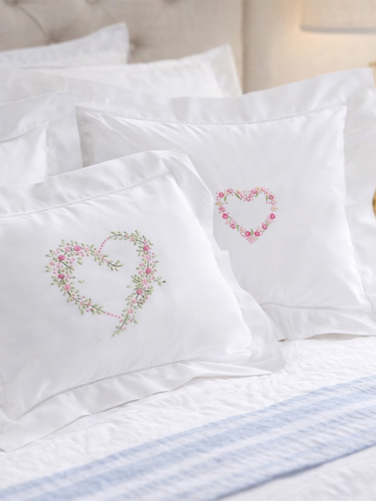 White pillows with embroidered heart designs on a bed.