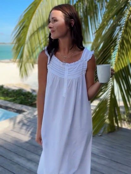 Woman in a white dress standing by a pool with palm trees in the background