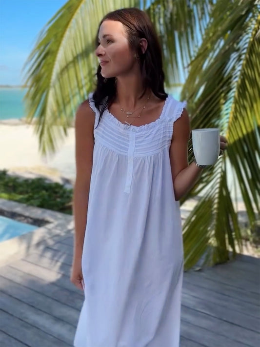 Woman in a white dress standing by a pool with palm trees in the background