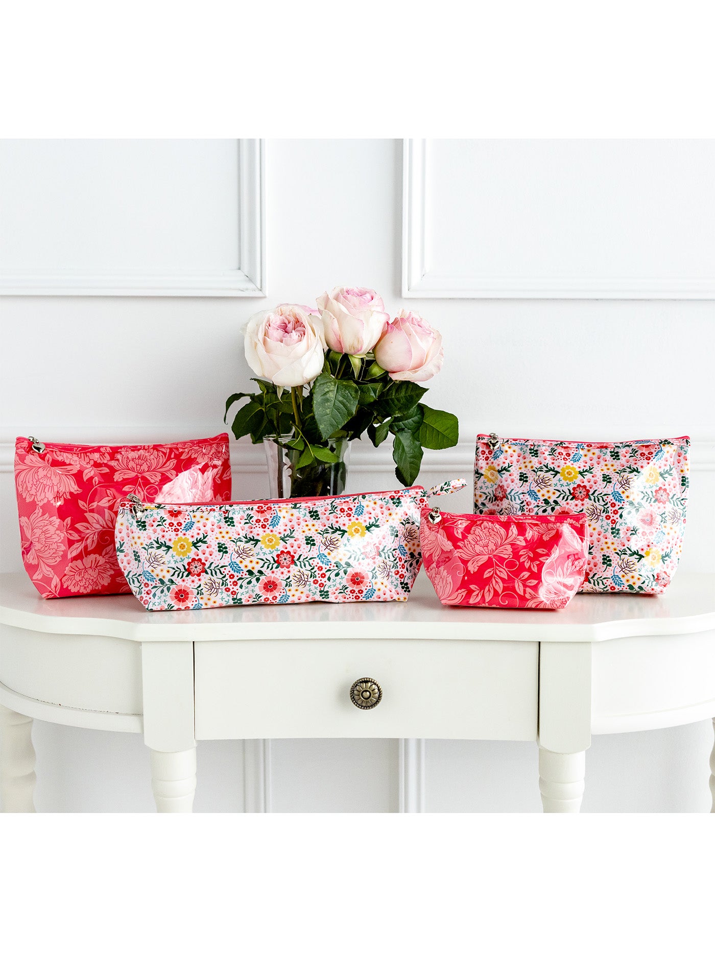 Floral-patterned makeup bags on a white surface with a vase of flowers.