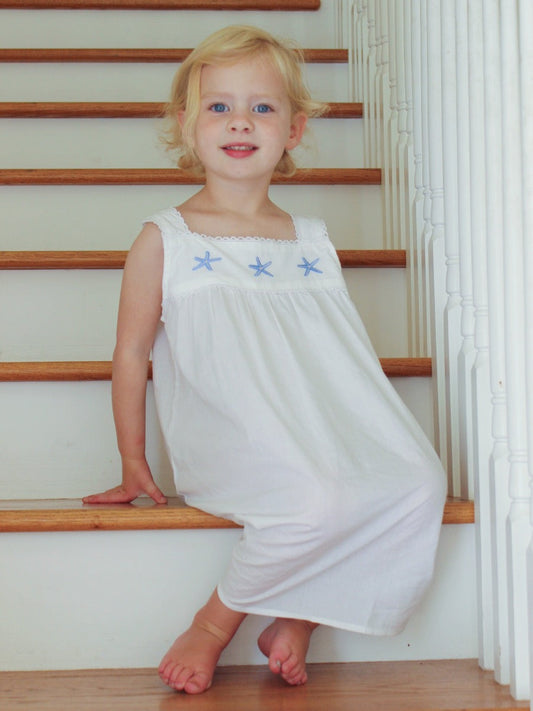 Young girl in a white dress with star designs sitting on wooden stairs.